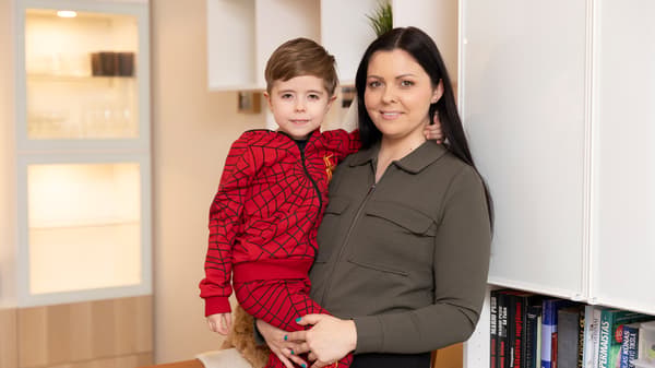 Mother holding son in modern living room with bookshelf.