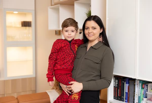 Mother holding son in modern living room with bookshelf.