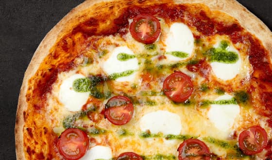 Mozzarella Pizza topped with mozzarella pearls, cherry tomatoes, pesto and cheese on a tomato sauce base