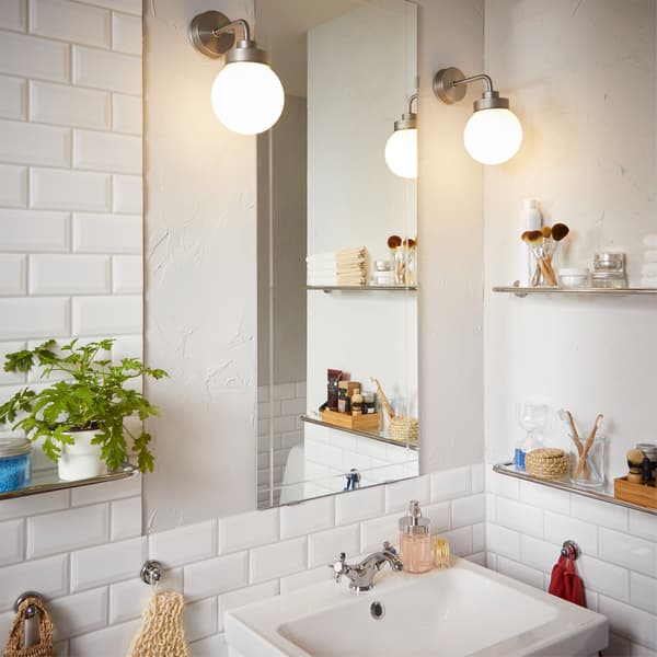 مرآة مثبتة على الحائط مع مصباح حائط واحد على كل جانب يوفّر إضاءة متساوية عند الوقوف أمامها.