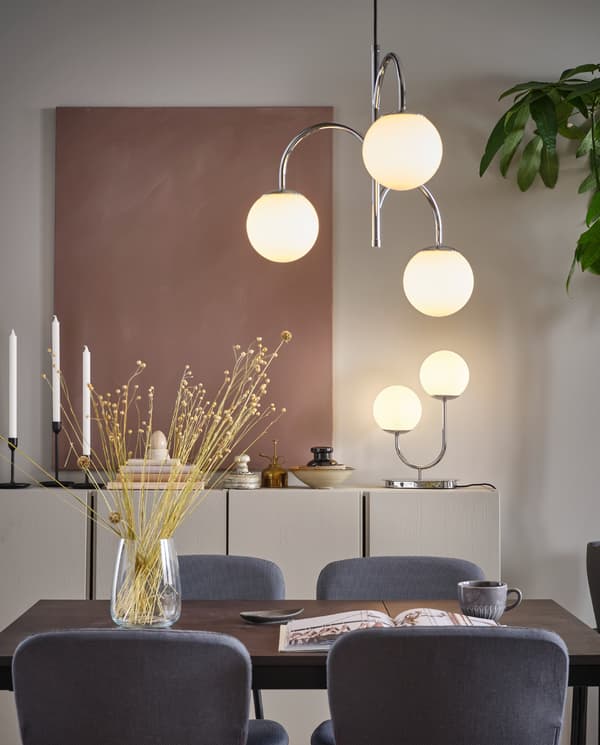 مصباح معلق 3 أذرع SIMRISHAMN مطلي بالكروم، معلق فوق طاولة طعام ومصباح طاولة SIMRISHAMN على خزانة.