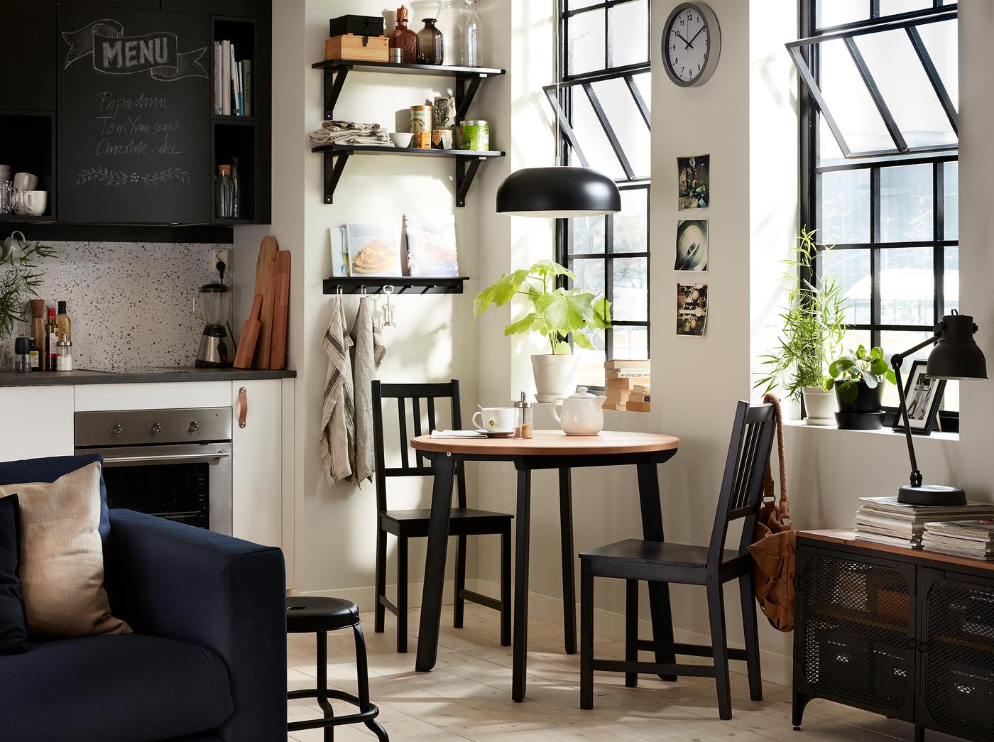 مطبخ أسود وأبيض به طاولة مستديرة صغيرة وكرسيان في الزاوية.