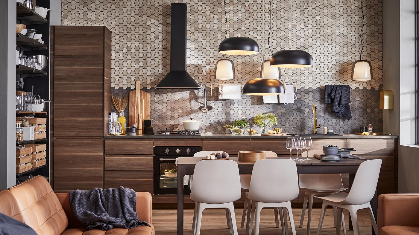 مطبخ بخزائن بني داكن شكل خشب الجوز، وثلاثة مصابح معلقة سوداء وطاولة بلون بني داكن وستة كراسي.