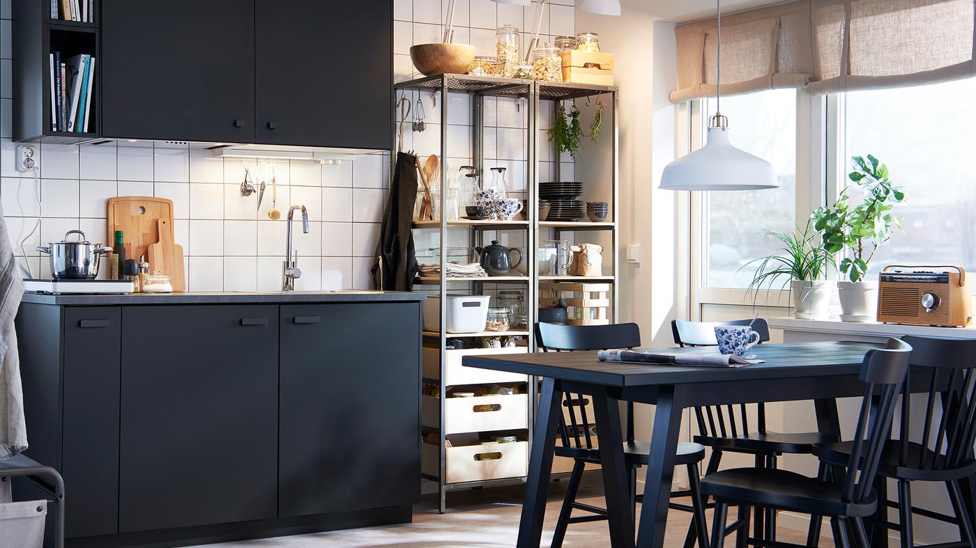 مطبخ بسيط أحادي اللون مع الخزائن داكنة اللون، وطاولة وكراسي سوداء، ورفوف معدنية مفتوحة.