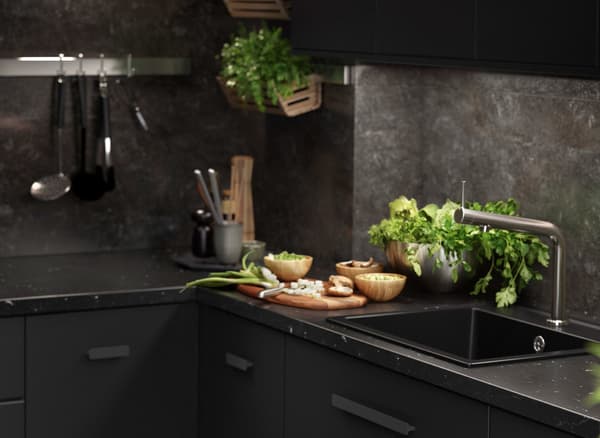 مطبخ KUNGSBACKA أسود مع رخام يحتوي على أدوات مطبخ وأعشاب طازجة.