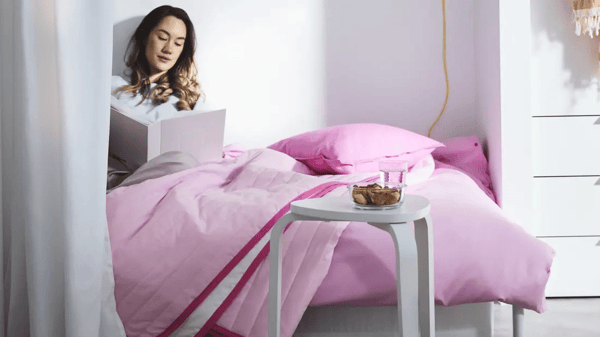 Muchacha en la cama estudiando cubierta en sabanas rosadas