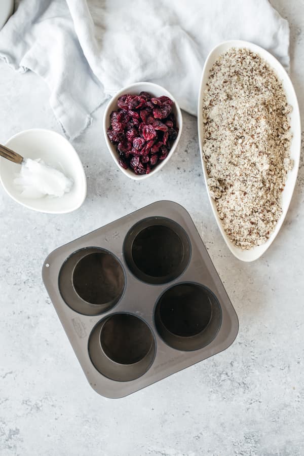 Muffinform, Schalen mit Cranberries, Mehl und Reis auf heller Oberfläche, Backzubehör im Hintergrund.