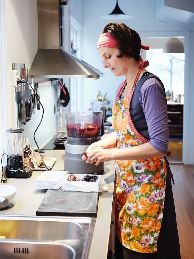 Mujer en la cocina con un delantal de flores naranjas y amarillas, cocinando con un cuchillo.