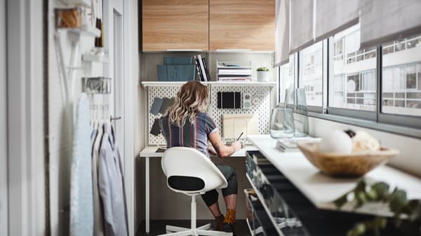 Mujer sentada en su espacio de trabajo escribiendo en el escritorio en una silla blanca redonda.