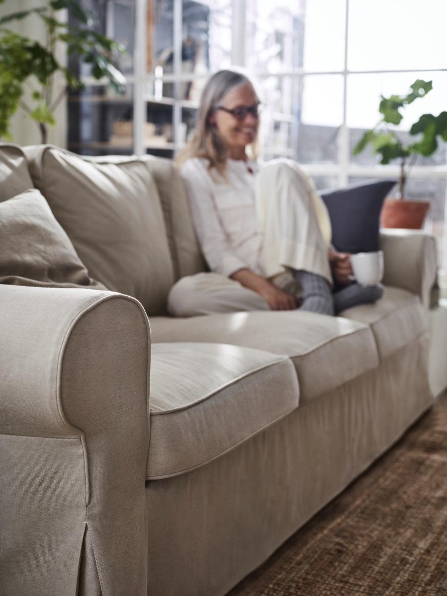 Mujer sentada en un sofá beige EKTORP con un cojín gris oscuro, tomado café en un living