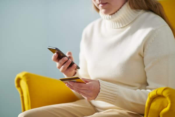 Mujer sentada sobre un sillón amarillo mirando su celular.