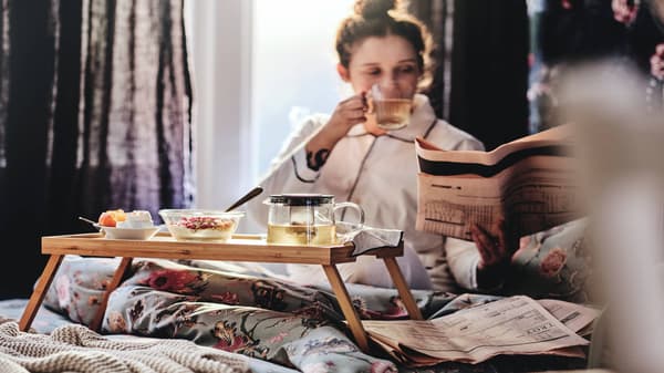 Mujer tomando desayuno en su cama mientras lee
