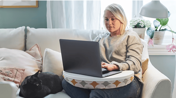 Mujer utilizando un computador sentada sobre un sillón.