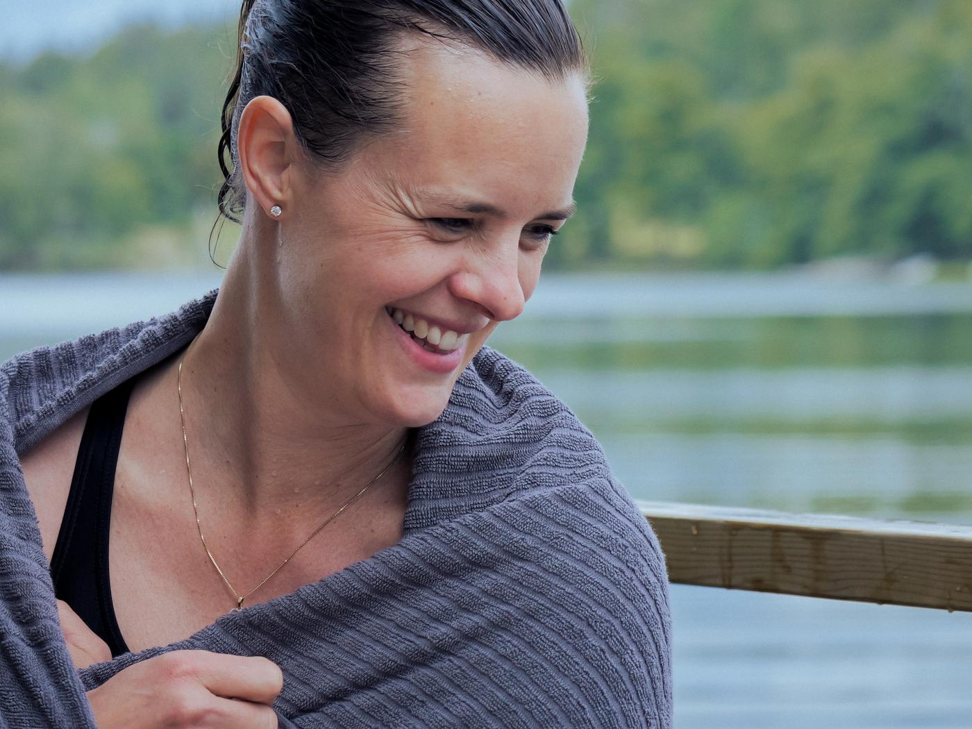 Mulher a sorrir e embrulhada numa toalha VÅGSJÖN após um mergulho no lago.