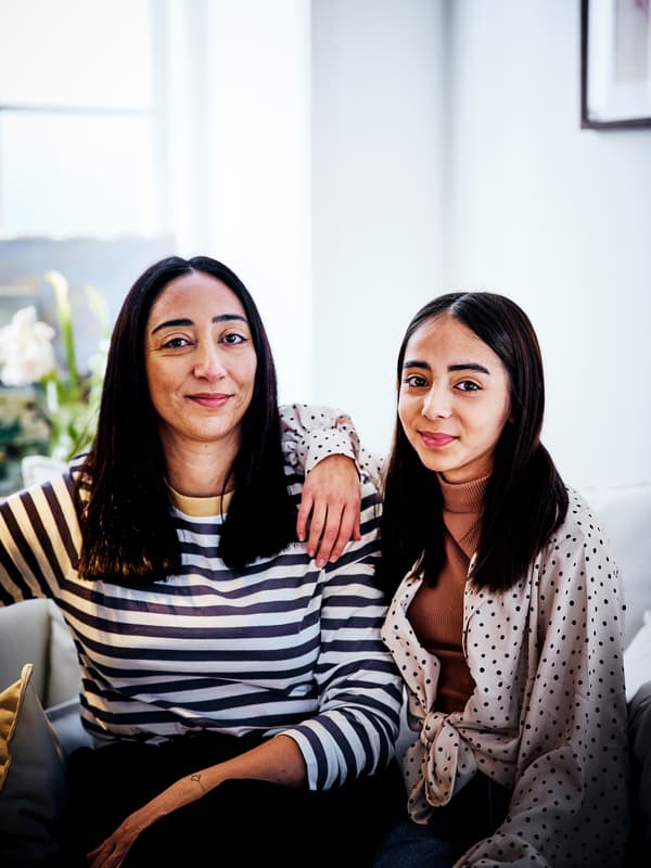 Mulher e rapariga sentadas lado a lado numa sala luminosa com paredes brancas e uma janela atrás.