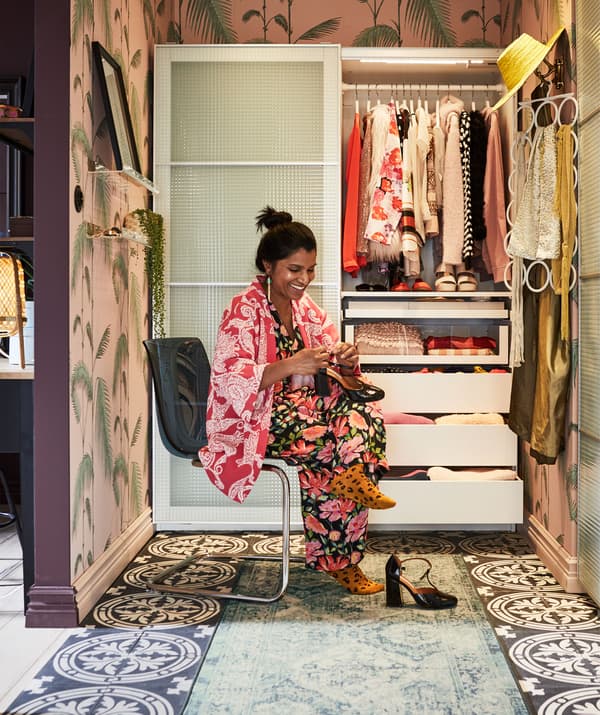 Mulher sentada numa cadeira, num recanto colorido e decorado com um roupeiro à medida, com uma porta deslizante meio aberta e acessórios pendurados na parede.