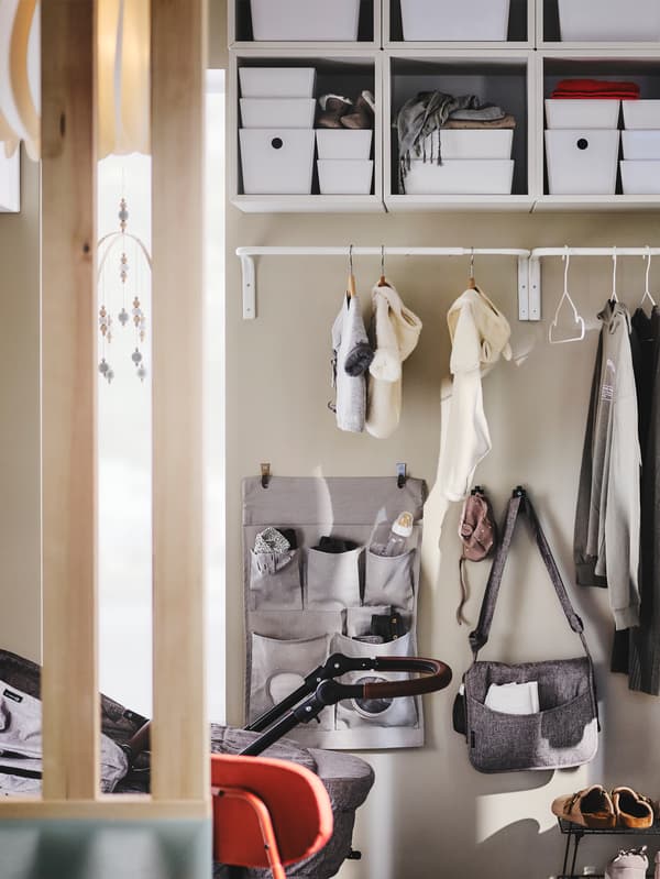 MULIG kledingroede met buitenkleding aan een wand in een hal, met een LEN hangende opberger en haken eronder.
