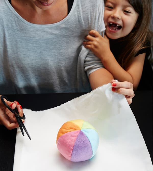 Muller envolvendo unha pelota de peluche cun mantel branco ante a mirada dun neno.