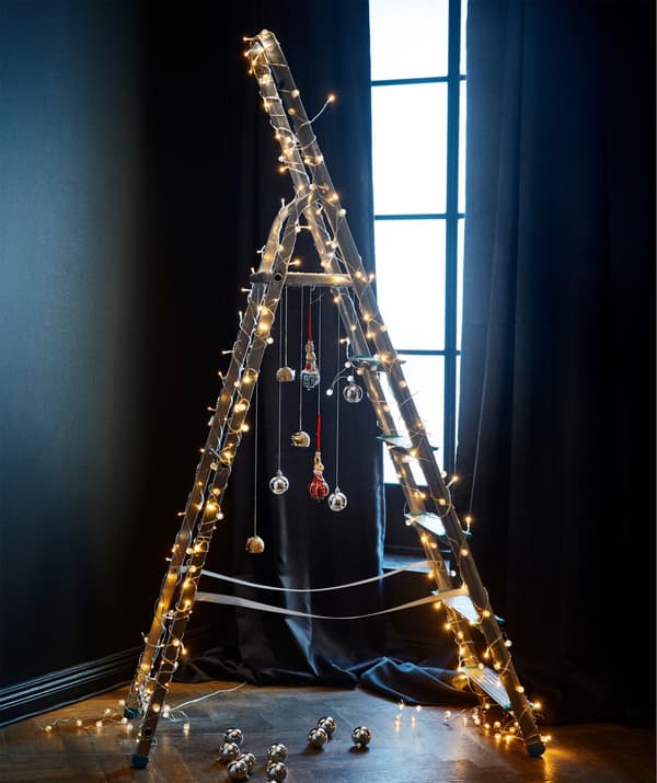 Multiple LED lighting chains adorning a step ladder in a partially darkened room.