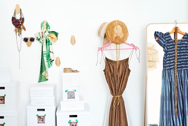 Mur de rangement avec des accessoires sur des crochets en bois, des boîtes à chaussures, des robes et des chapeaux sur un portemanteau et un miroir en pied.