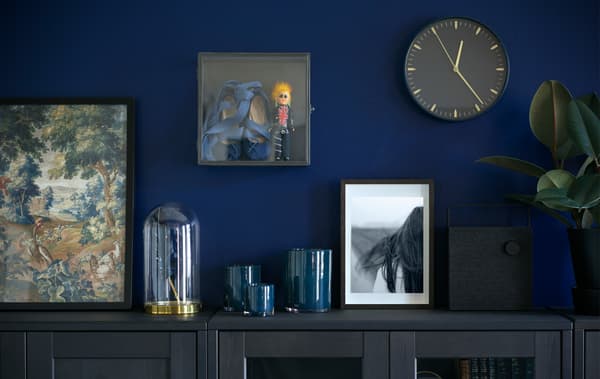 Mur peint en bleu accueillant une horloge, des cadres variés et la vitrine BARKHYTTAN.