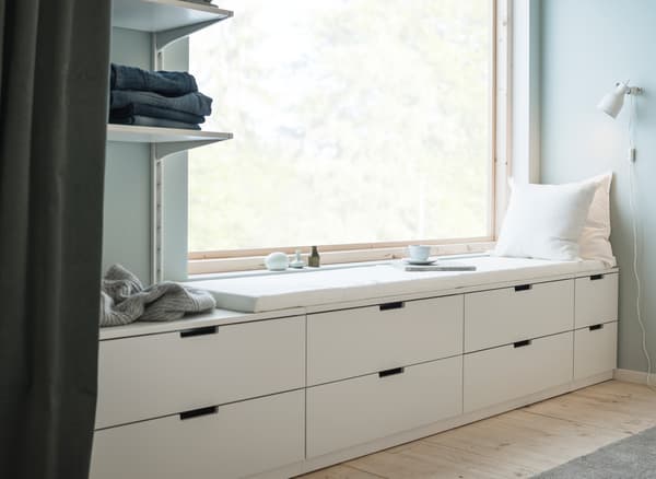 Mur percé d’une grande fenêtre et doté de plusieurs commodes blanches à deux tiroirs d’allure moderne.