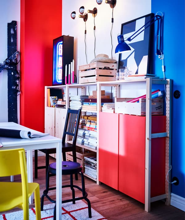 Mur rouge/blanc/bleu avec étagères et rangements en pin. Une table blanche est entourée de chaises et d'un tabouret.