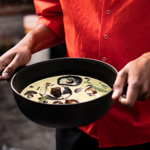 Mushroom soup served in the bottom part of a black ÖVERALLT pot with lid made from enamelled cast iron with two handles.
