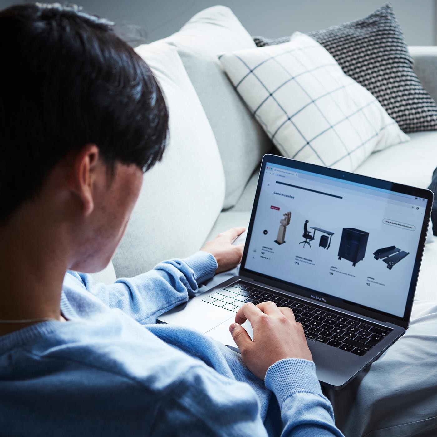 Muškarac leži na sofi u dnevnoj sobi sa laptopom u krilu i pretražuje sajt.