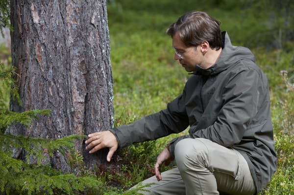 Muškarac s naočalama sjedi pokraj drva u šumi. Pregledava deblo dodirivanjem.