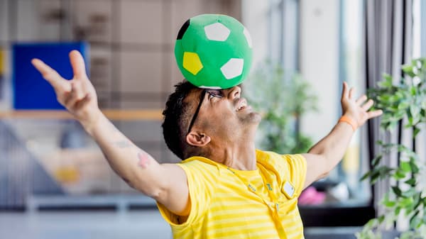 Muž balancujúci plyšovú futbalovú loptu na hlave.