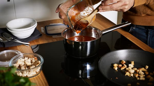 Muž nalieva paradajkovú omáčku z dózy IKEA 365+ do hrnca na sporáku.