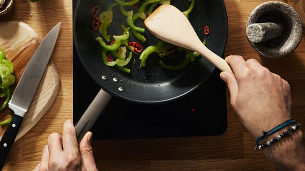 Muž pripravuje vegetariánske jedlo so zelenými a červenými paprikami na prenosnej indukčnej varnej doske TILLREDA.