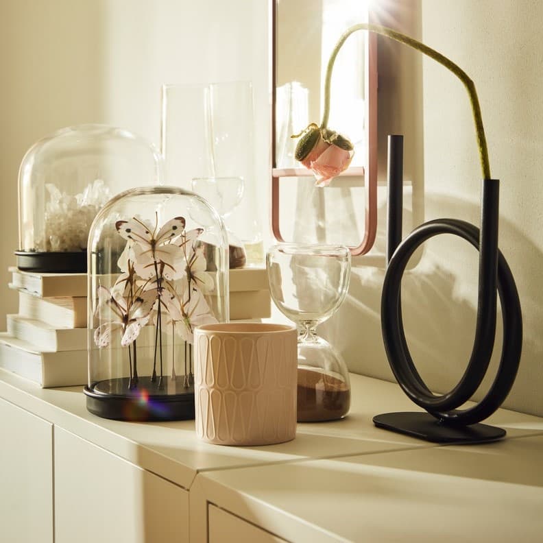 Na białej komodzie stoją dekoracje takie jak świeczniki, wazony i kwiaty.