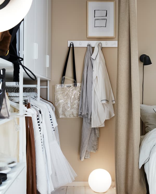 Na białym wieszaku LURT/GUBBARP z sześcioma haczykami, zamontowanym na ścianie obok otwartej szafy wiszą wietrzące się ubrania.