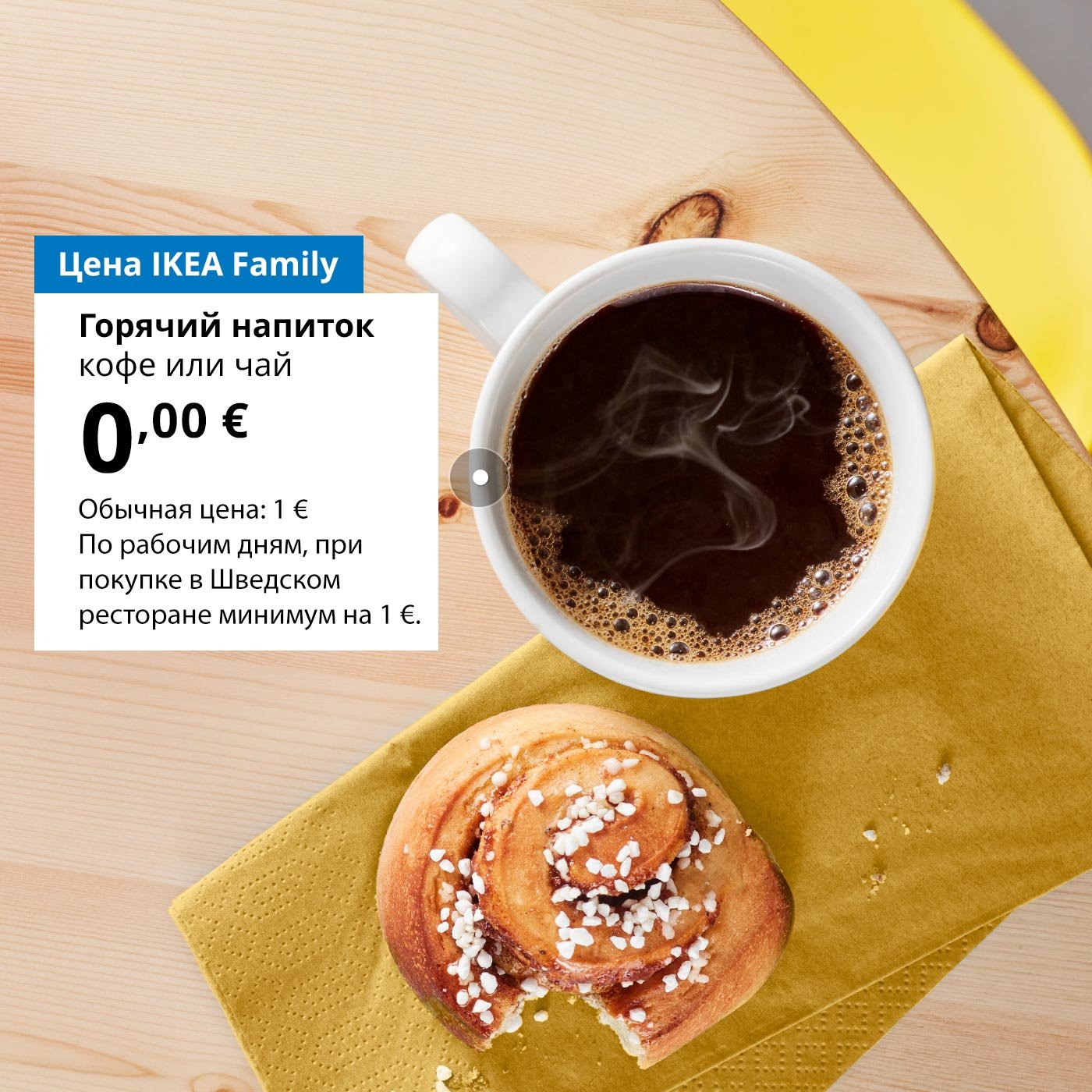 На деревянном столе лежит недоеденная булочка с корицей и кружка кофе. Рядом с кружкой, на белом фоне, размещено предложение для членов клуба IKEA Family: горячий напиток (кофе или чай) за 0 €, обычная цена 1 €.