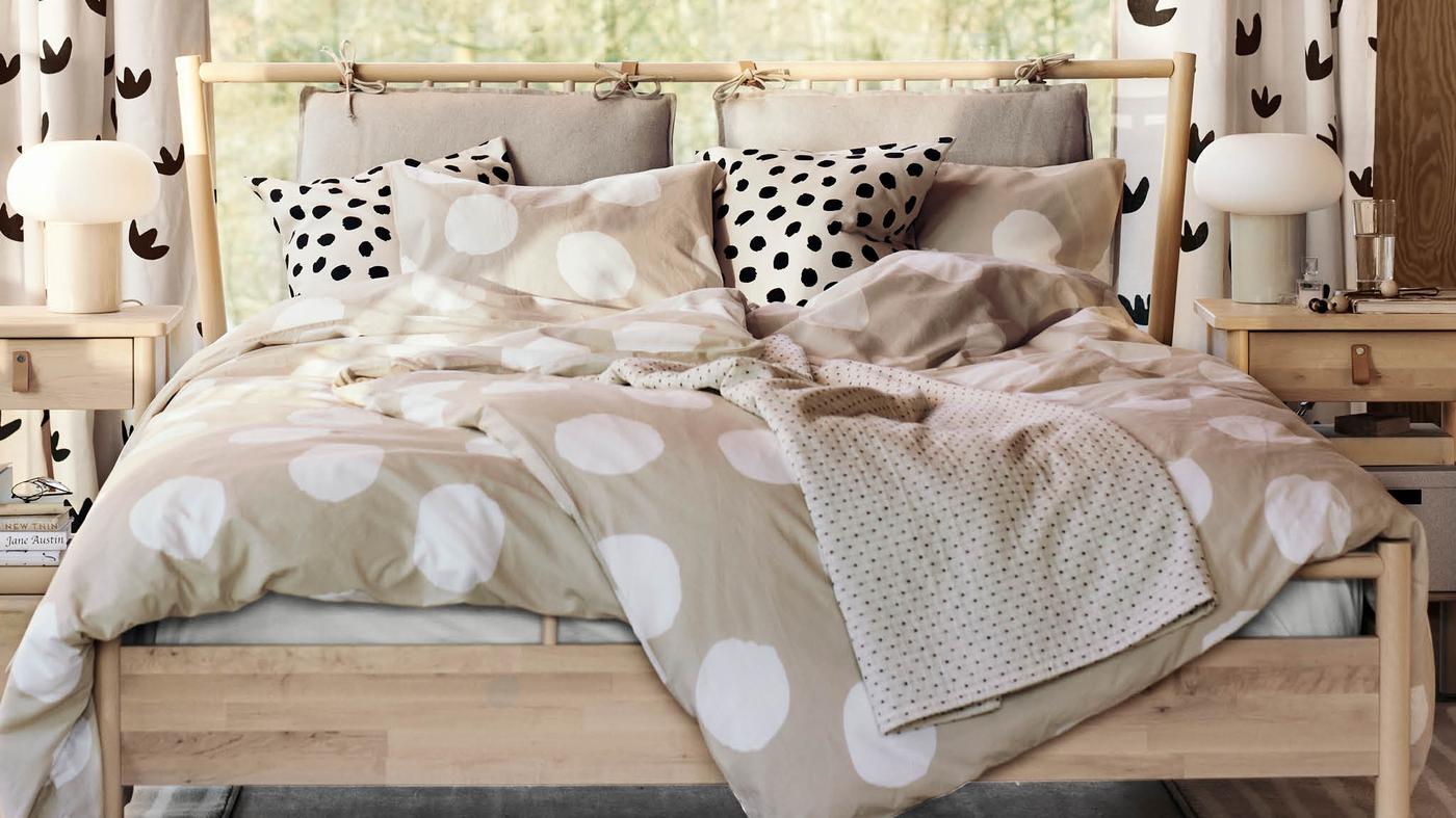 Na dvojlůžku BJÖRKSNÄS leží přikrývky v povlečení KLYNNETÅG a dva polštářky v povlaku ODDNY, za dvěma nočními stolky BJÖRKSNÄS visí pár závěsů NÄCKROSMOTT.