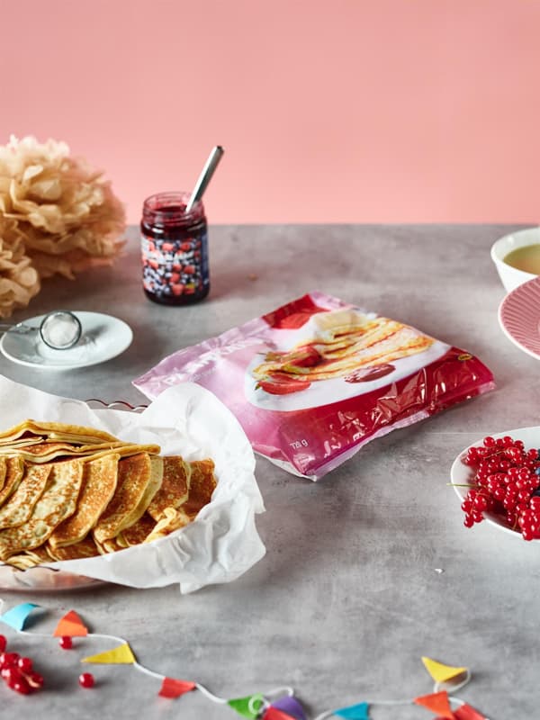 Na pracovní desce je vidět prázdný obal od palačinek, které leží na talíři, vedle stojí sklenice s džemem.