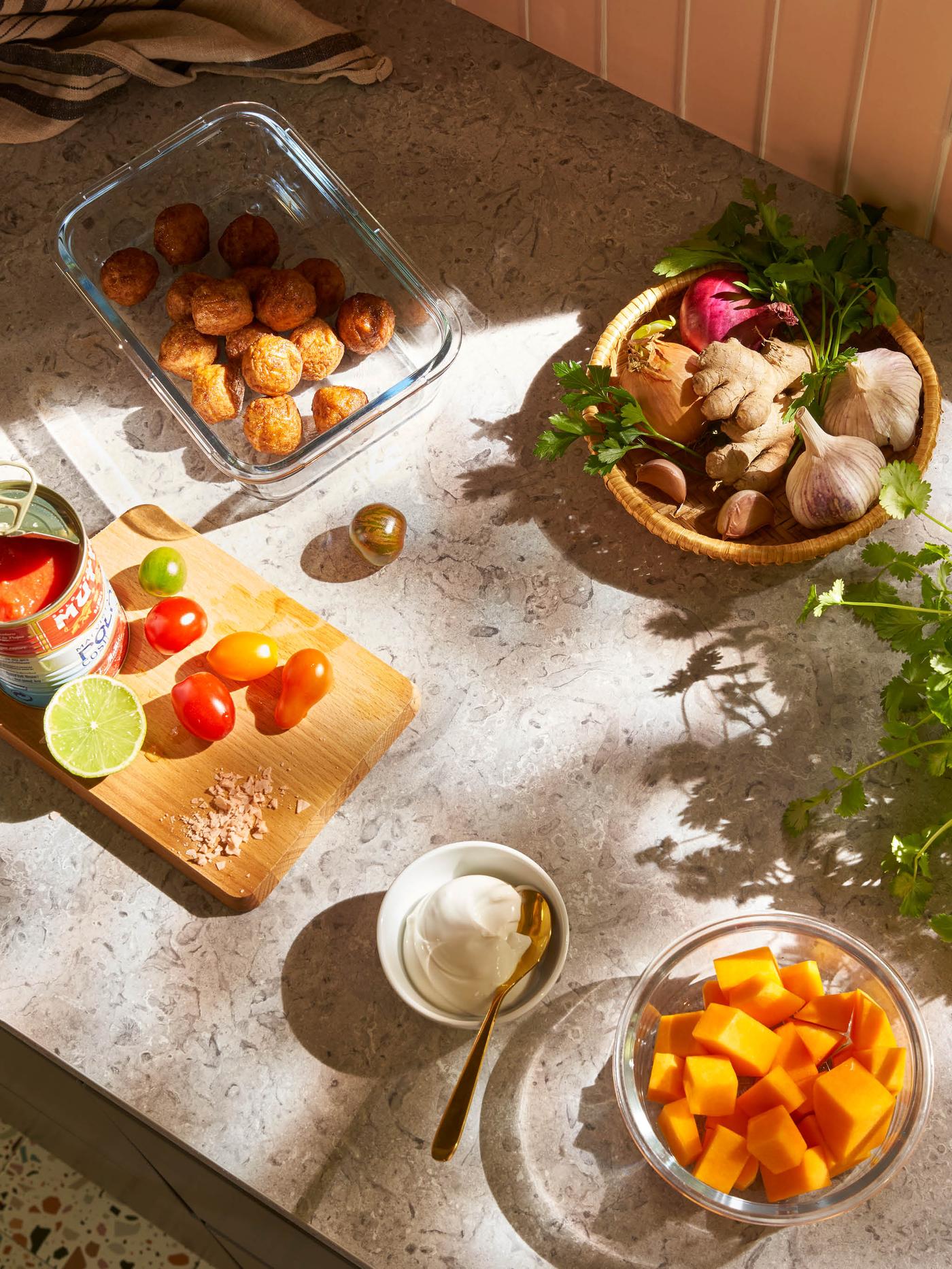 Na prkénku stojí plechovka drcených rajčat a několik čerstvých rajčat, vedle je skleněná dóza IKEA 365+ s bezmasými kuličkami, miska joigurtu a miska VARDAGEN s nakrájenou dýní.