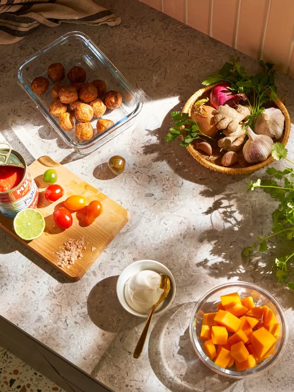 Na prkénku stojí plechovka drcených rajčat a několik čerstvých rajčat, vedle je skleněná dóza IKEA 365+ s bezmasými kuličkami, miska joigurtu a miska VARDAGEN s nakrájenou dýní.