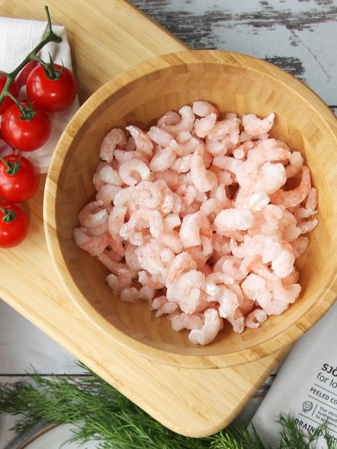 Na prkénku STOLHET leží bambusová miska BLANDA MATT plná krevet, vedle větvičky cherry rajčat.