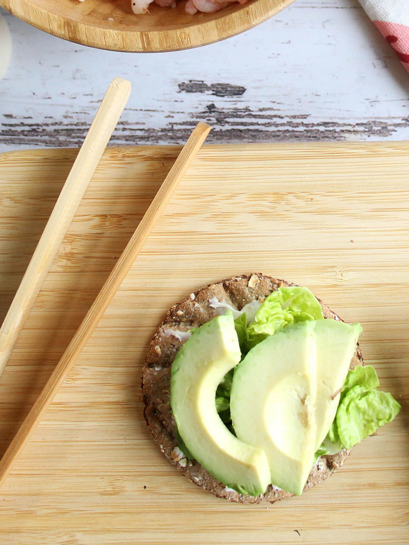 Na prkénku STOLHET leží plátek křehkého chleba KNÄCKEBRÖD FLERKORN s listovým salátem a plátky avokáda.