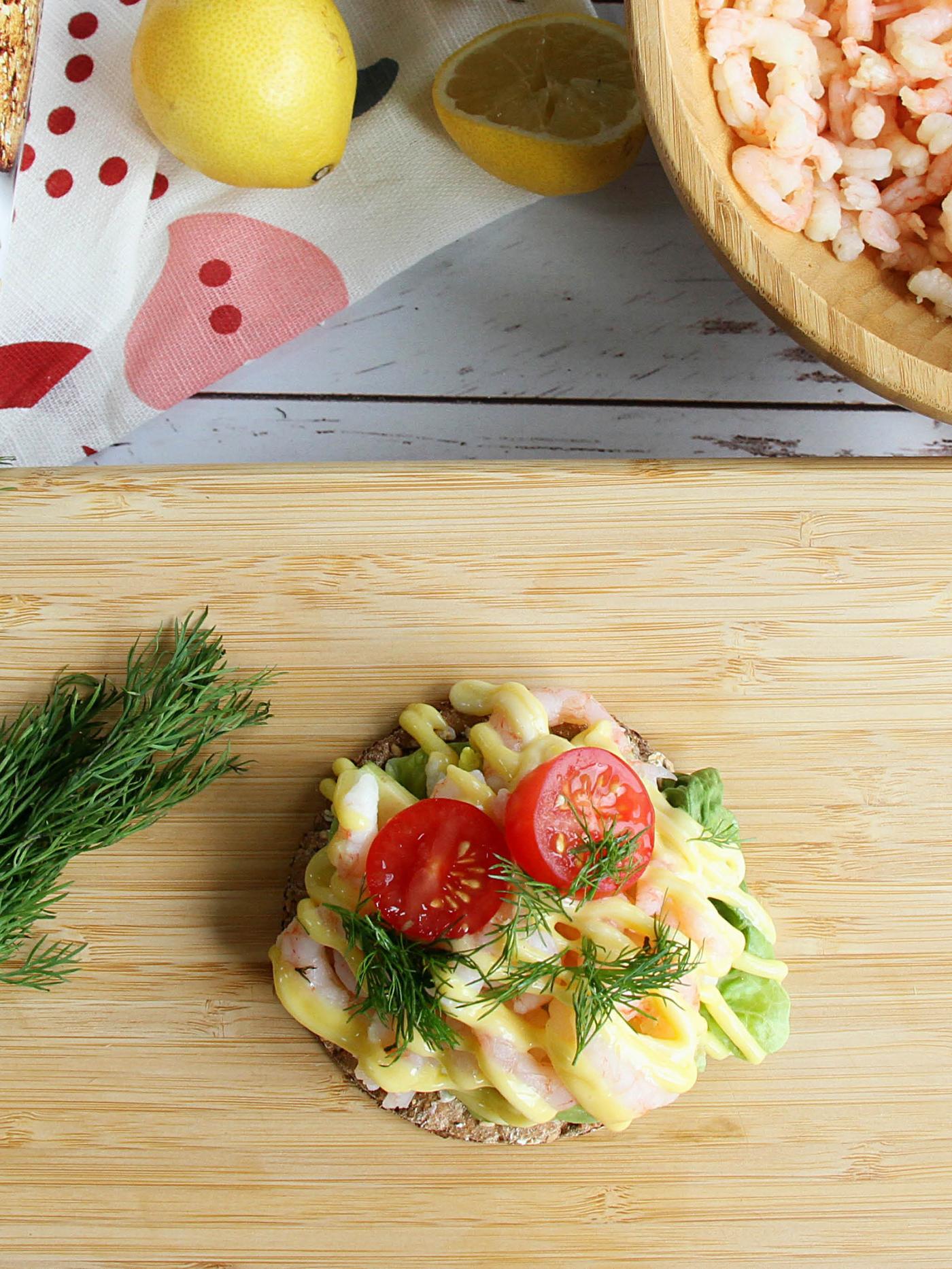 Na prkénku STOLHET leží plátek křehkého chleba KNÄCKEBRÖD FLERKORN s krevetami, vedle leží svazek kopru, v pozadí je bambusová miska BLANDA MATT plná krevet a citrony.