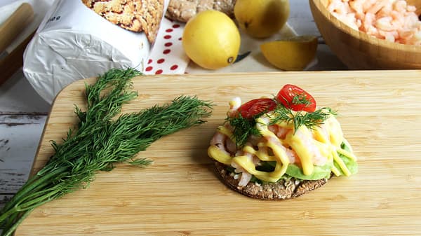 Na prkénku STOLHET leží plátek křehkého chleba KNÄCKEBRÖD FLERKORN s krevetami, vedle leží svazek kopru, v pozadí je bambusová miska BLANDA MATT plná krevet, citróny a balení křehkého chleba KNÄCKEBRÖD FLERKORN.