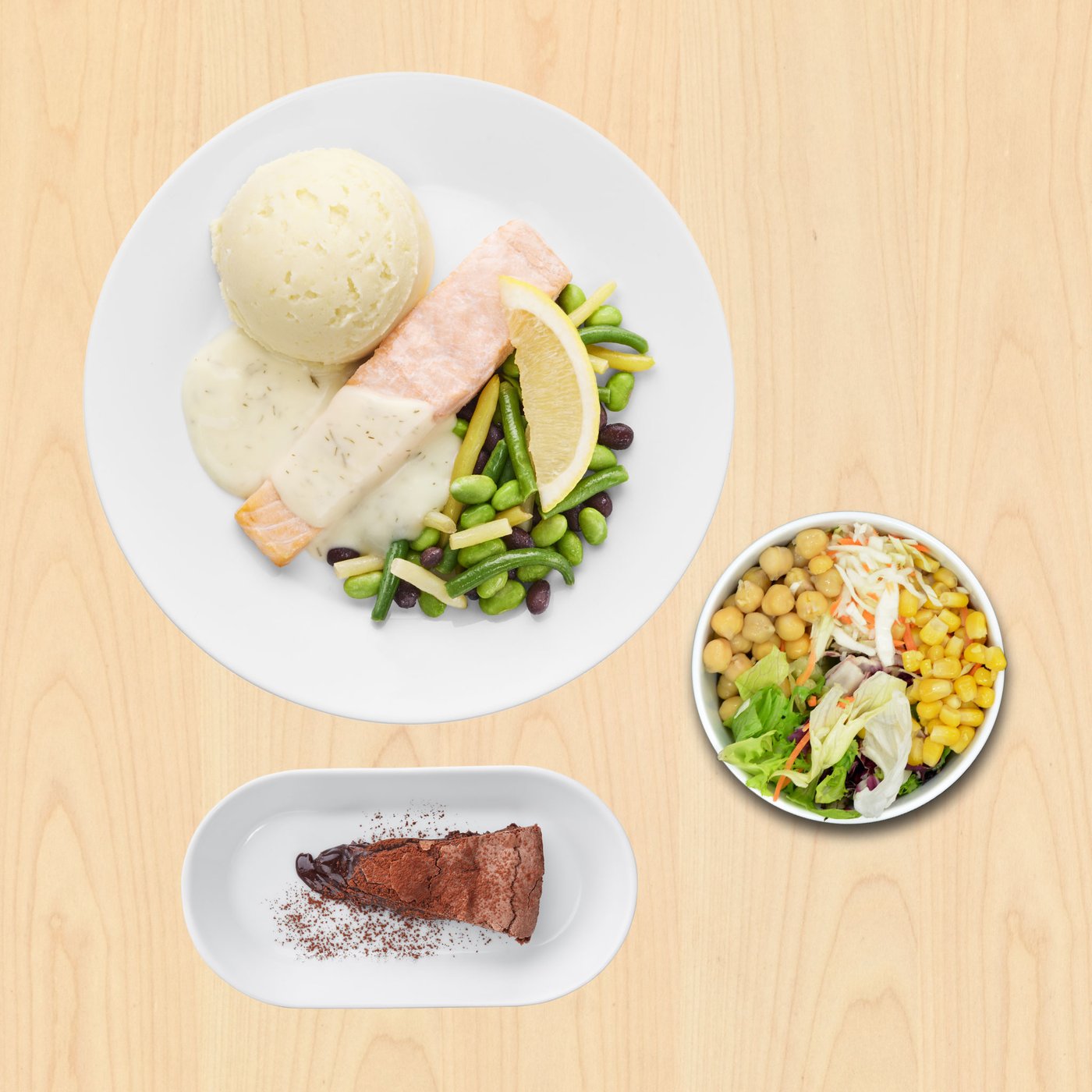 Na slici je obrok poslužen na drvenoj podlozi: na velikom tanjuru nalazi se file lososa s kriškom limuna, pire krumpir i mješavina zelenog povrća s bijelim umakom. Uz to je zdjelica salate s kukuruzom i slanutkom te desert – komad čokoladne torte.