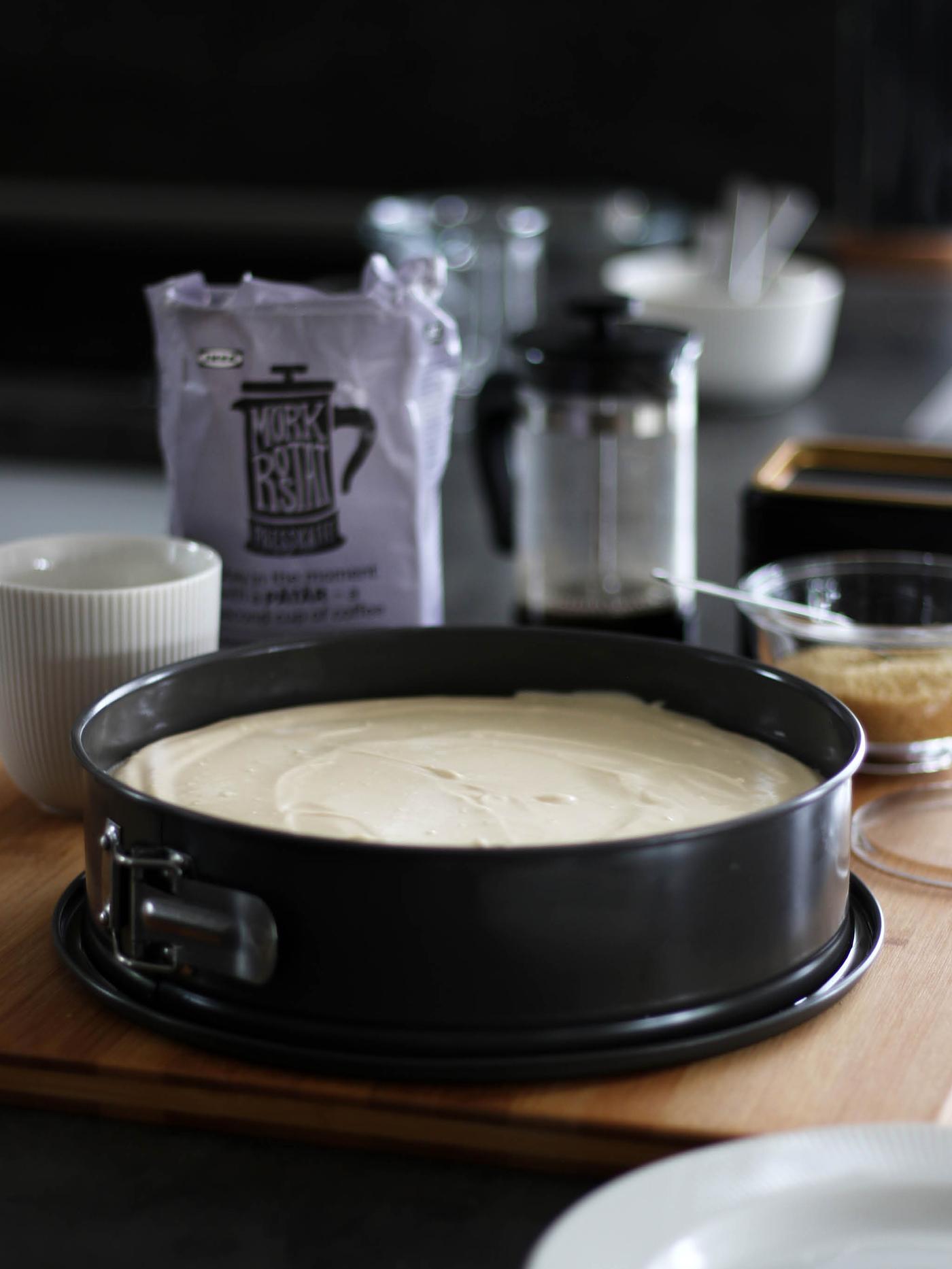 Na stole leží dortová forma HEMMABAK s cheescakem, za ní stojí koncice na kávu UPPHETTA, balíček kávy PÅTÅR, bílá hrnek OFANTLIGT a cukřenka s třtinovým cukrem.