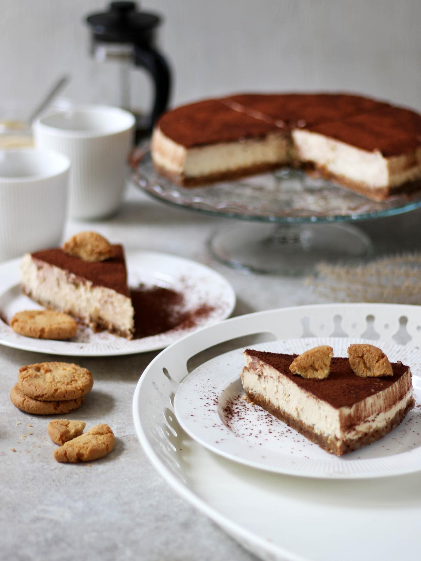 Na stole leží dva dezertní talíře OFANTLIGT s porcemi cheescake, za nimi stojí dva hrnky OFANTLIGT, servírovací stojan ARV BRÖLLOP a konvice na kávu UPPHETTA.