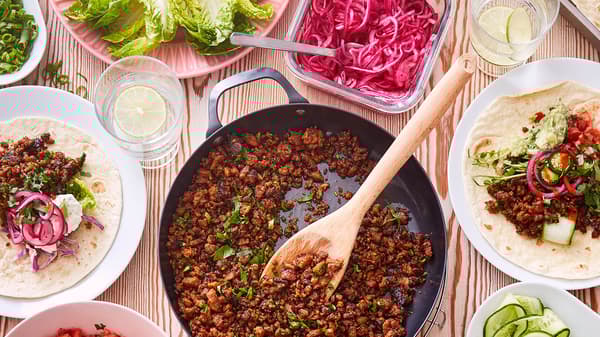 Na stole leží pánev VARDAGEN plná bezmasé směsi VÄRLDSKLOK na Tacos, okolo jsou talíře s tortillami a miska s naloženou červenou cibulí.