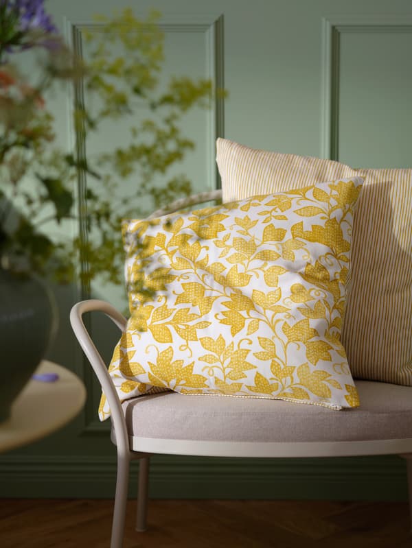 Na světle šedobéžovém křesle ISMANTORP leží dva polštáře ve žluto-bílém povlaku FJUNKLOCKA.