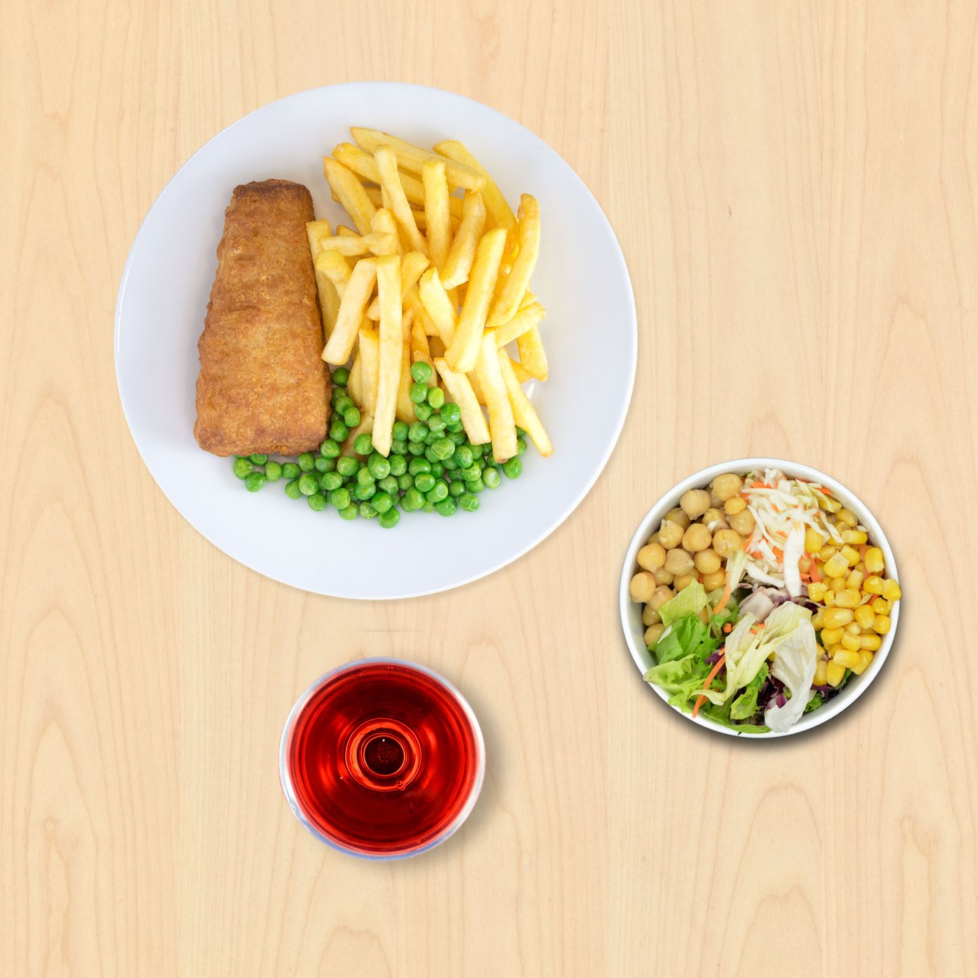 Na tanjuru su pržena riba, pomfrit i zeleni grašak. Pokraj je zdjelica miješane salate s kukuruzom i slanutkom te čaša crvenog napitka na drvenoj podlozi.